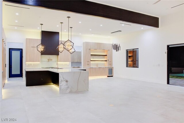 kitchen featuring beam ceiling, modern cabinets, light brown cabinetry, a kitchen island with sink, and light stone countertops