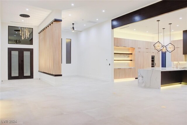 unfurnished living room with french doors, a notable chandelier, recessed lighting, a sink, and baseboards