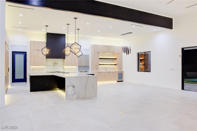 kitchen featuring light brown cabinetry, an island with sink, modern cabinets, and light stone countertops