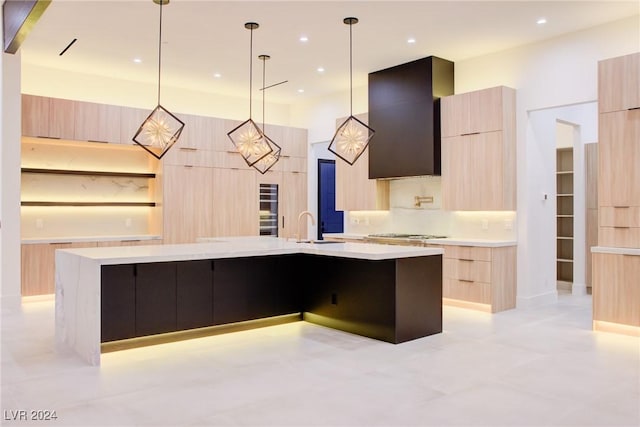 kitchen featuring wall chimney exhaust hood, a large island, modern cabinets, light countertops, and light brown cabinetry