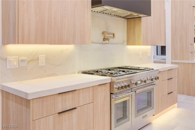 kitchen with light countertops, range with two ovens, wall chimney range hood, and light brown cabinetry