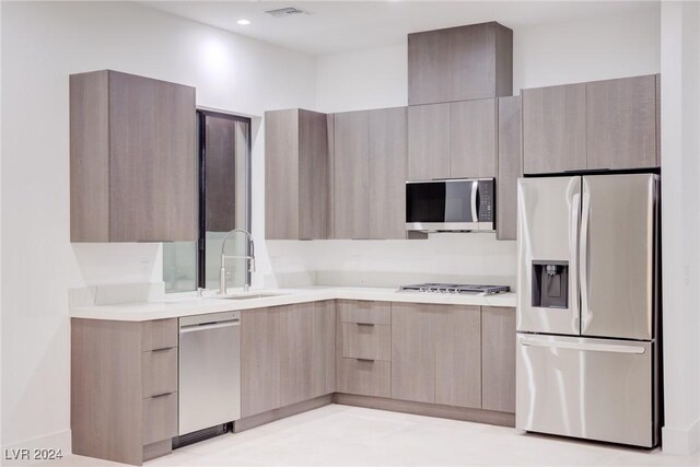 kitchen with modern cabinets, stainless steel appliances, light countertops, light brown cabinets, and a sink