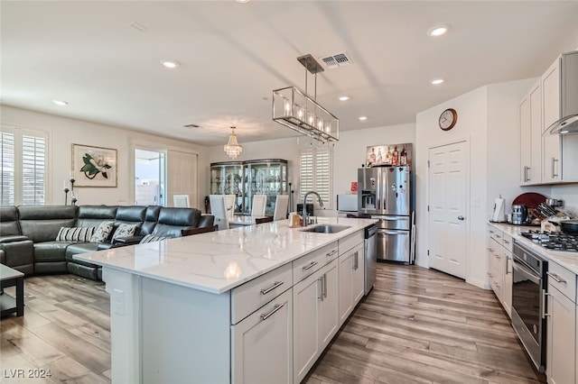 kitchen featuring sink, an island with sink, white cabinets, light hardwood / wood-style flooring, and stainless steel appliances