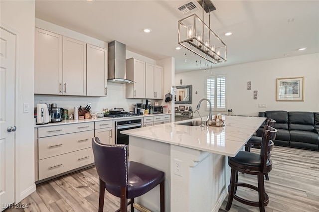 kitchen featuring appliances with stainless steel finishes, a kitchen breakfast bar, wall chimney exhaust hood, a center island with sink, and sink