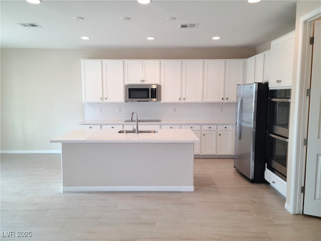 kitchen featuring sink, decorative backsplash, a center island with sink, white cabinets, and appliances with stainless steel finishes