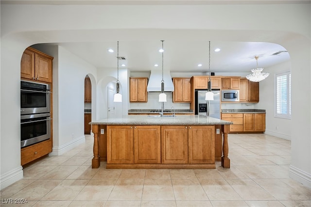 kitchen featuring light stone countertops, appliances with stainless steel finishes, pendant lighting, an inviting chandelier, and a kitchen island with sink