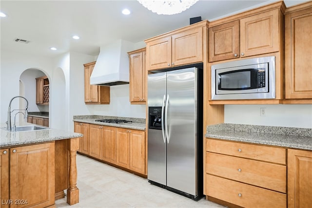 kitchen featuring appliances with stainless steel finishes, custom range hood, sink, and light stone countertops