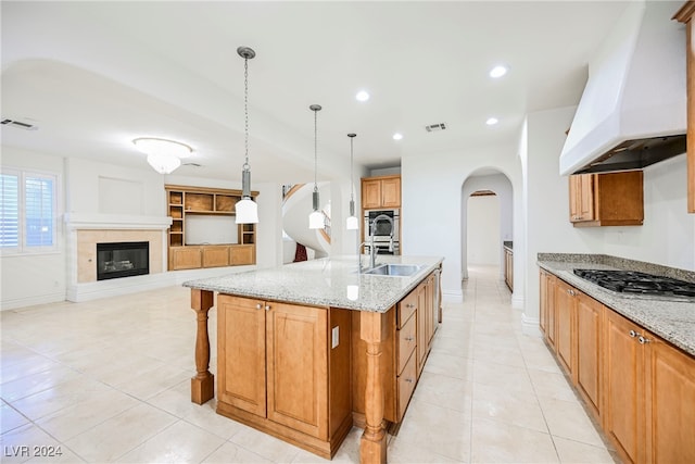 kitchen featuring a center island with sink, stainless steel gas stovetop, custom range hood, pendant lighting, and sink