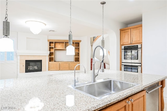 kitchen with light stone countertops, decorative light fixtures, sink, and stainless steel double oven