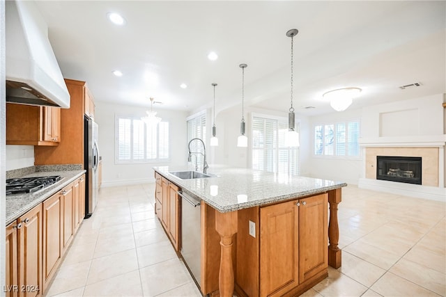 kitchen with appliances with stainless steel finishes, sink, decorative light fixtures, custom exhaust hood, and a kitchen island with sink