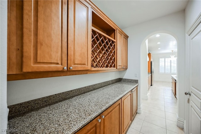 bar featuring stone counters, stainless steel refrigerator, and light tile patterned floors