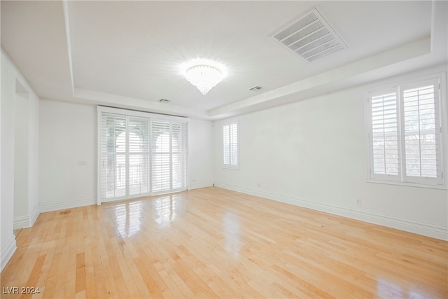 empty room featuring a notable chandelier, light hardwood / wood-style floors, and a raised ceiling