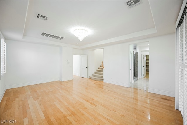 empty room with light wood-type flooring and a raised ceiling