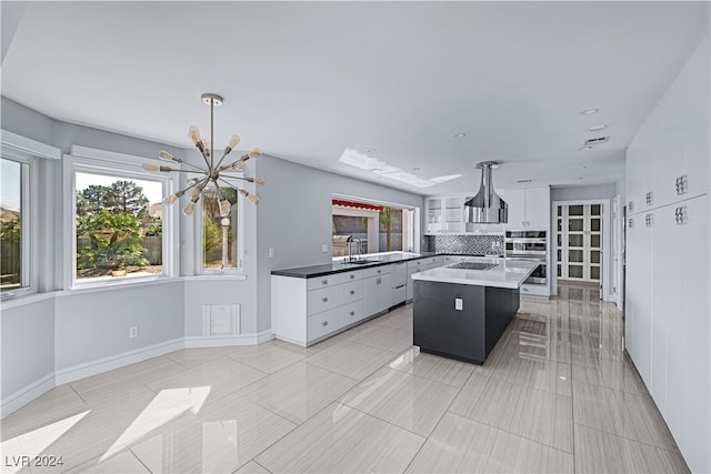 kitchen featuring a kitchen island, double oven, hanging light fixtures, white cabinetry, and backsplash