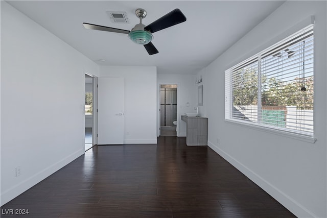 unfurnished bedroom with dark wood-type flooring, ceiling fan, a walk in closet, and ensuite bath