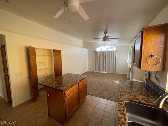 kitchen featuring a kitchen island, ceiling fan, light carpet, sink, and dark stone counters