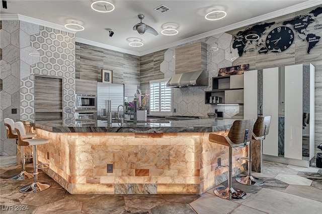 kitchen featuring wall chimney exhaust hood, stainless steel microwave, and ornamental molding