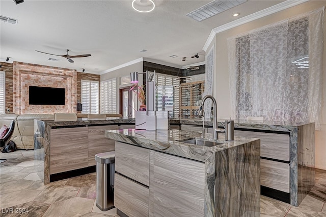 kitchen with dark stone counters, a center island, sink, ornamental molding, and ceiling fan