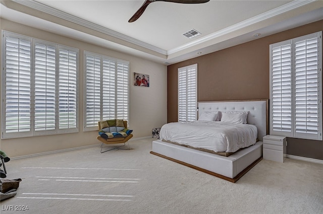 carpeted bedroom with a tray ceiling, multiple windows, ceiling fan, and crown molding