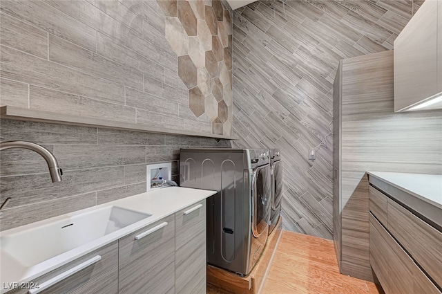 clothes washing area featuring cabinets, tile walls, sink, washer hookup, and light hardwood / wood-style flooring