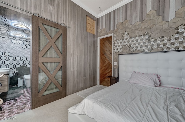 carpeted bedroom with a barn door, ensuite bathroom, wood walls, and ornamental molding