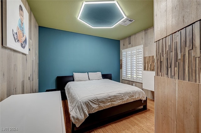 bedroom with wooden walls and light hardwood / wood-style flooring