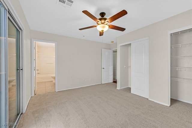 unfurnished bedroom with ceiling fan, light carpet, two closets, and ensuite bath