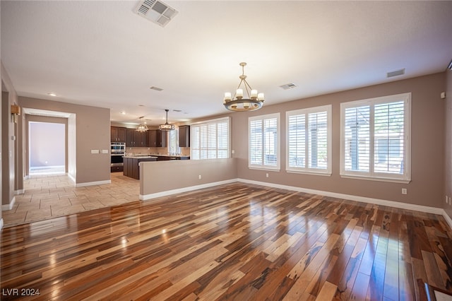 unfurnished living room featuring light hardwood / wood-style floors, a notable chandelier, and plenty of natural light