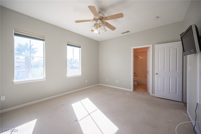 unfurnished bedroom with light carpet, a spacious closet, connected bathroom, and ceiling fan