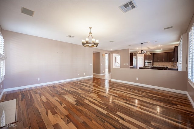 unfurnished living room with dark hardwood / wood-style flooring, a notable chandelier, and plenty of natural light