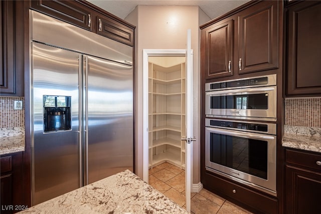 kitchen featuring light stone countertops, stainless steel appliances, and dark brown cabinets