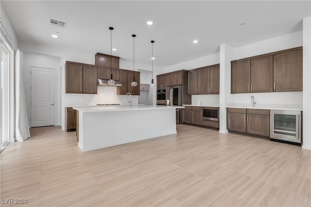 kitchen with sink, an island with sink, beverage cooler, hanging light fixtures, and stainless steel appliances