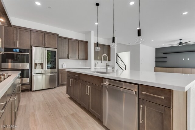 kitchen featuring pendant lighting, sink, an island with sink, appliances with stainless steel finishes, and dark brown cabinetry