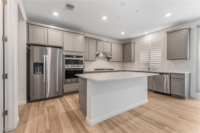 kitchen with gray cabinetry, stainless steel appliances, a center island, and light hardwood / wood-style flooring