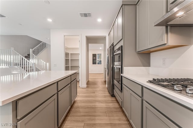 kitchen featuring ventilation hood, gray cabinetry, light hardwood / wood-style flooring, and stainless steel appliances