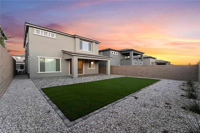 back house at dusk featuring a lawn and a patio area