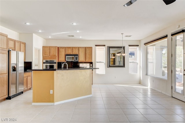 kitchen featuring appliances with stainless steel finishes, hanging light fixtures, light tile patterned floors, a kitchen island with sink, and sink