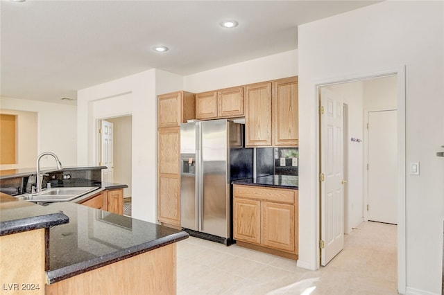 kitchen with light tile patterned flooring, tasteful backsplash, dark stone counters, sink, and stainless steel fridge with ice dispenser