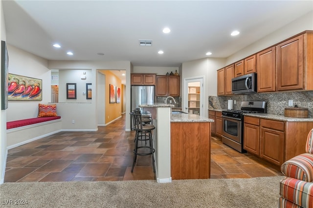 kitchen with appliances with stainless steel finishes, decorative backsplash, a breakfast bar, light stone countertops, and a center island with sink