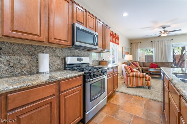 kitchen with light stone counters, ceiling fan, appliances with stainless steel finishes, light colored carpet, and decorative backsplash