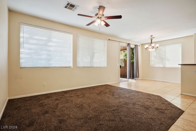 carpeted spare room featuring ceiling fan with notable chandelier