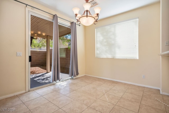 tiled spare room featuring an inviting chandelier