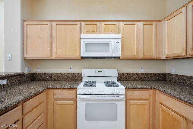 kitchen featuring dark stone countertops, white appliances, and light brown cabinets