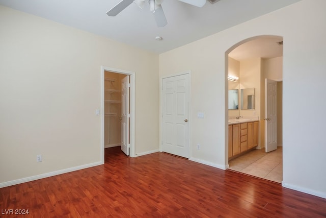 unfurnished bedroom with ceiling fan, a closet, a spacious closet, ensuite bath, and light hardwood / wood-style floors