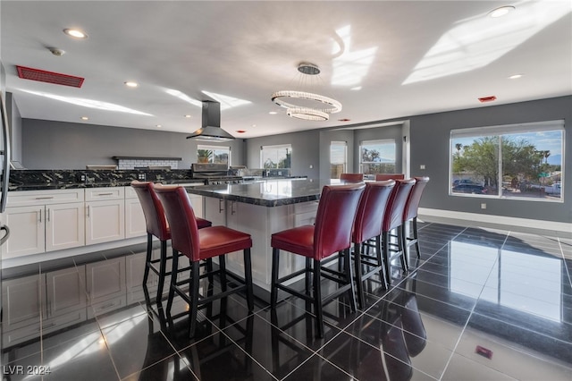 kitchen with a kitchen island, white cabinets, a breakfast bar, dark stone counters, and range hood