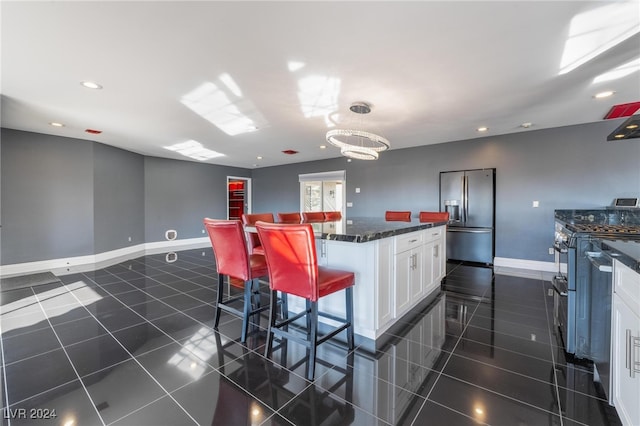 kitchen featuring a breakfast bar area, dark tile patterned flooring, stainless steel appliances, white cabinets, and a center island