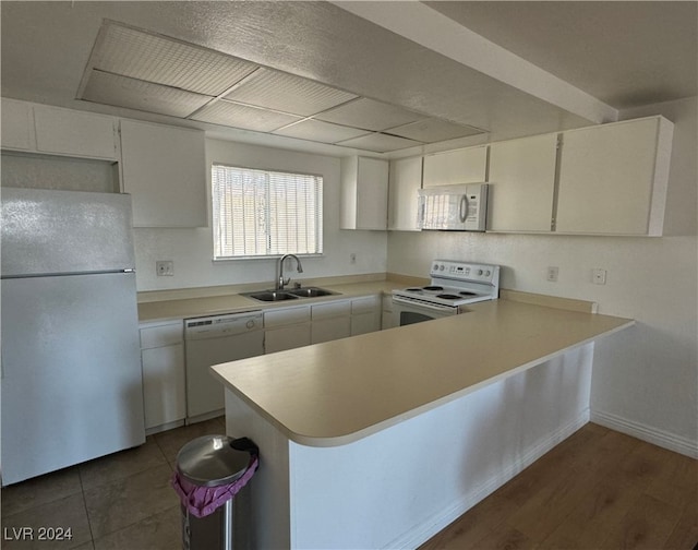 kitchen with sink, kitchen peninsula, white appliances, white cabinetry, and dark hardwood / wood-style floors