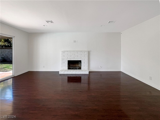 unfurnished living room with dark hardwood / wood-style flooring and a brick fireplace