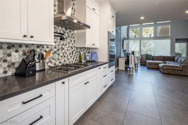 kitchen featuring backsplash, white cabinetry, wall chimney range hood, and stainless steel appliances