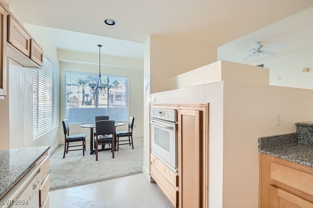 kitchen with ceiling fan with notable chandelier, dark stone counters, hanging light fixtures, and oven